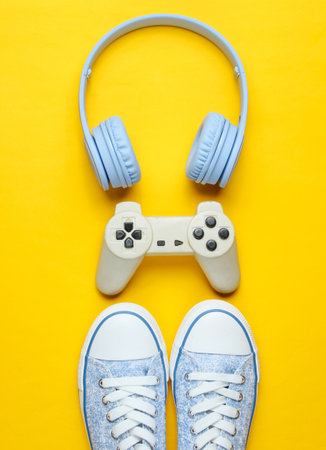 Gamer concept. Gamepad with headphones, sneakers on yellow background. Top view, creative flat layの写真素材