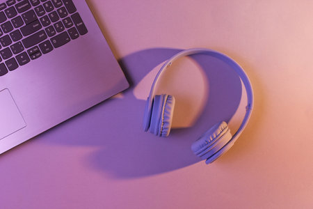 Modern laptop, wireless headphones. Gadgets. Orange purple neon light, ultraviolet. Top view, minimalismの写真素材