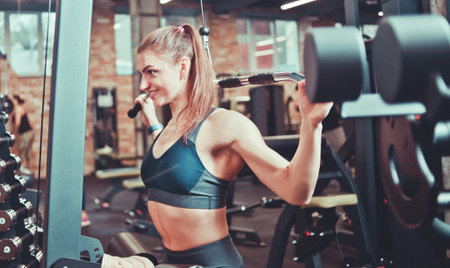 Athlete woman training her back, arms and shoulders with exercise machine in a gym, sport conceptの写真素材