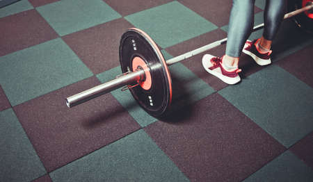 Woman trains in the gym with a barbell. Powerlifting. Heavy barbell on the floor and female legsの写真素材