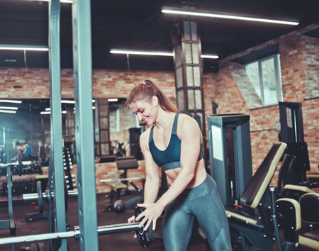 Athletic woman putting disk to barbell in gymの写真素材