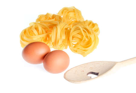 Raw dry tagliatelle noodle, eggs, wooden spoon close up isolated on white backgroundの写真素材
