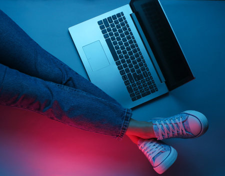 Night online work at laptop. Freelance concept. Hacker. A woman is sitting on the floor with laptop. Dark neon glow. Top viewの写真素材