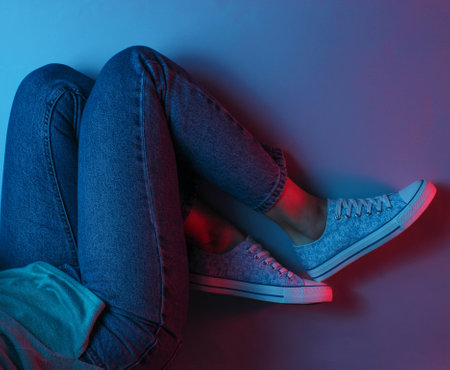 The concept relax. Women's legs in jeans and sneakers. Neon light. Top view.の写真素材