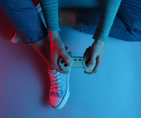 Concept gamer. Nightlife. Leisure. Woman sitting on the floor and holding gamepad. Neon red blue...