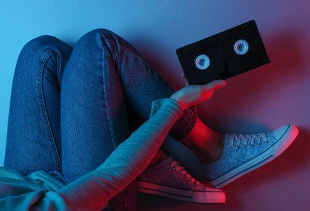 Retro wave still life. Women in jeans and sneakers holding video tapes. Neon light. top viewの写真素材