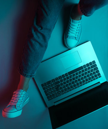 Night online work at laptop. Freelance concept. Hacker. A woman is sitting on the floor with laptop. Dark neon glow. Top viewの写真素材