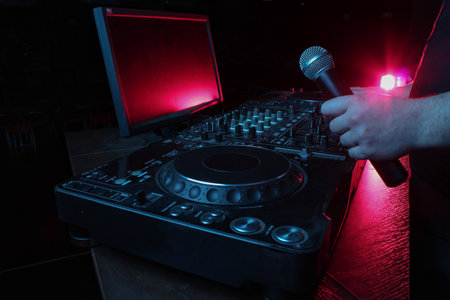 Night club, nightlife concept. Disco. DJ hands hold microphone and mixing DJ remote. Neon lightの写真素材