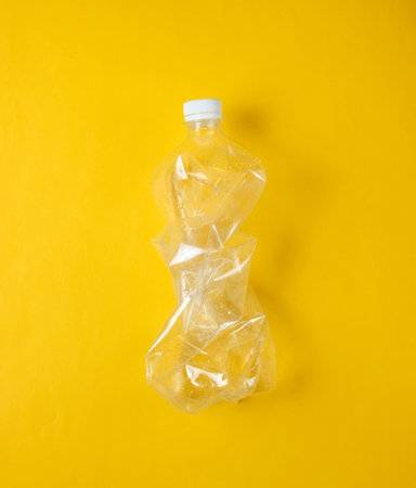 Minimalistic ecological concept. Crumpled plastic bottle on yellow background. Environmental plastic...