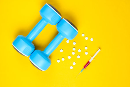 Doping in sport. Anabolic steroid. Sports Pharmacy. Plastic dumbbells, syringe, pills on yellow background. Top view.の写真素材