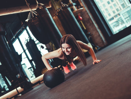 Woman doing push ups whith medicine ball  at dark gymの写真素材