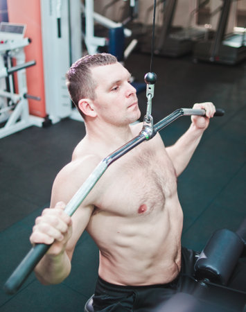 Athlete man in the gym doing vertical thrust. Exercise for muscles of the back.