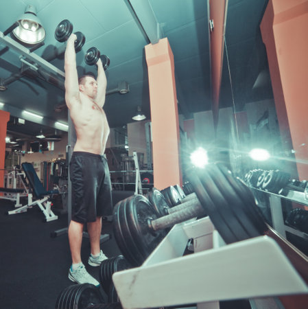 Athletic man with naked torso doing dumbbell bench exercises standing near rack with dumbbells in a gymの写真素材