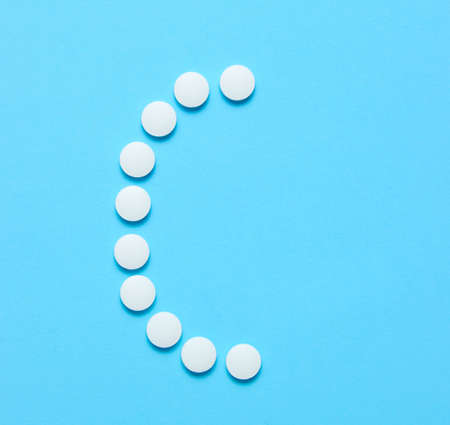 Vitamin C. Letter C from white pills on blue background. Minimalistic medical concept. Top view.の写真素材