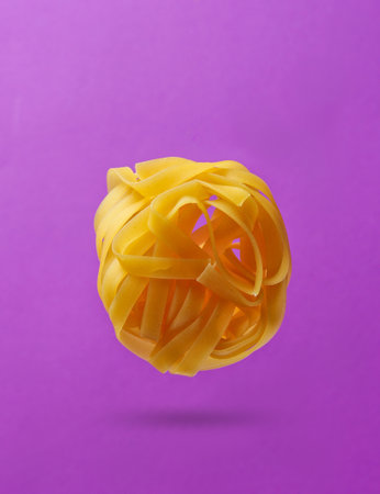 Minimalism italian food concept. Raw tagliatelle noodles on purple background. 3D photo with shadowの写真素材
