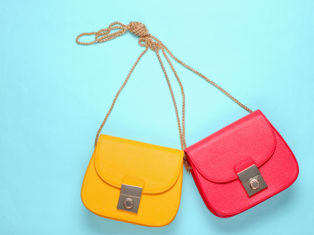 Red and yellow two leather bags with chain on yellow background. Minimalism fashion concept. Top...