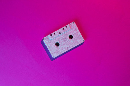 Retro wave style audio cassette with neon pink-violet light. 80s. Top view