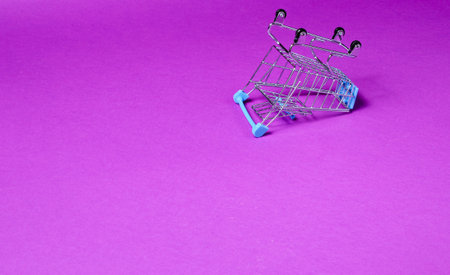 Minimalist shopping concept. Empty inverted miniature shopping trolley on purple background. Copy spaceの写真素材