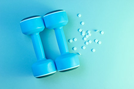 Minimalism sports pharmacology concept. Two blue plastic dumbbells and white anabolic pills, blue green holographic light. Top viewの写真素材