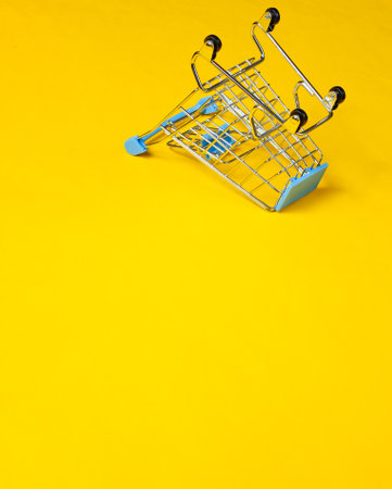 Minimalist shopping concept. Empty inverted miniature shopping trolley on yellow background. Copy spaceの写真素材