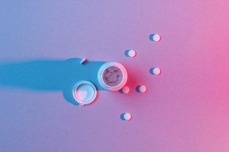 Minimalism medical concept. Small bottle with antidepressants white pills, neon red-blue light. Sleeplessness. Top viewの写真素材