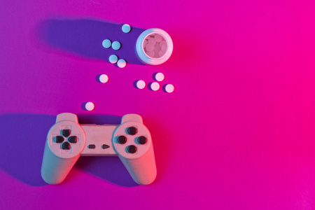 The concept of gaming addiction. Gamepad and pill bottle, neon pink light. Top view, minimalism
