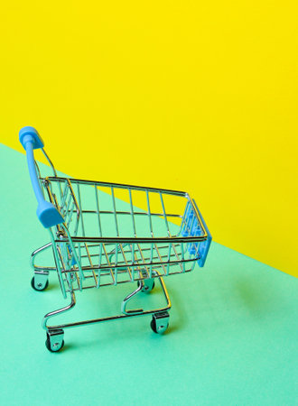 Minimalist shopping concept. Toy shopping trolley on pastel yellow-blue backgroundの写真素材