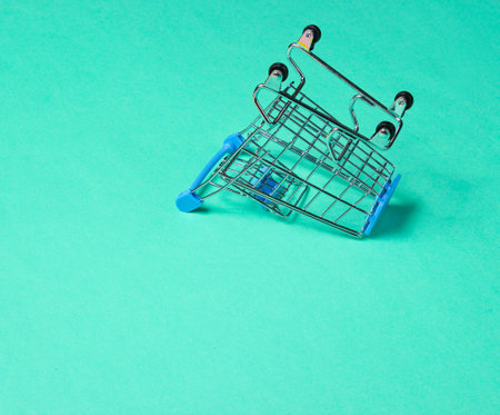 Minimalist shopping concept. Empty inverted miniature shopping trolley on blue backgroundの写真素材
