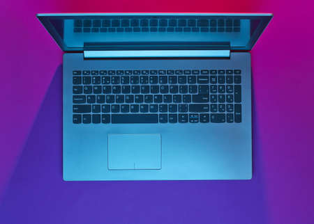 Modern laptop with vibrant gradient pink blue neon  lights. Minimalism. Top viewの写真素材