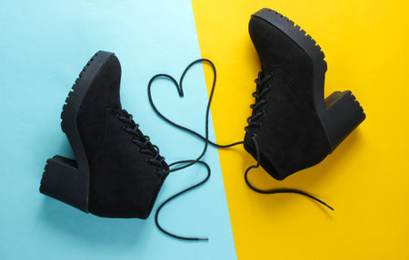Black suede boots with heart-shaped laces on blue yellow background. Top viewの写真素材