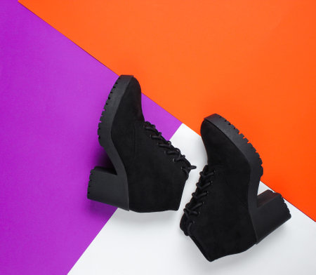 Black suede boots on a triangular colored paper background.の写真素材