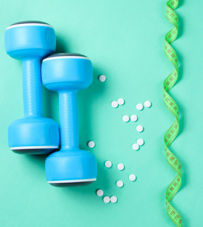 Sport weight loss concept. Dumbbells, ruler, pills on a blue background. Minimalism. Top viewの写真素材