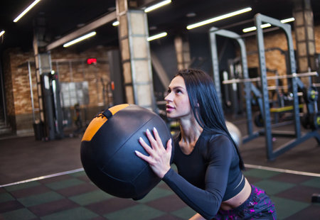 Concentrated fit woman in sportswear doing exercise with med ball in gymの写真素材