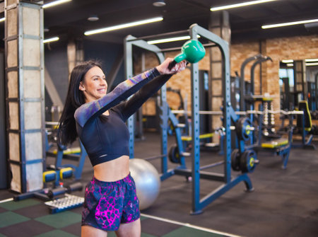 Young sporty brunette doing jerk exercise with kettlebell. in the gym. Free-weight strength training, functional trainingの写真素材