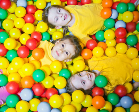 Three happy little kids girls in ball pit smiling happily at camera while having fun in children play center. Top viewの写真素材