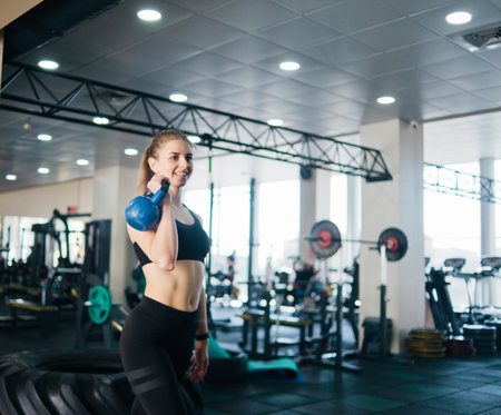 Young woman in sportswear lifts the kettlebell with one hand standing in the gym. Functional trainingの写真素材
