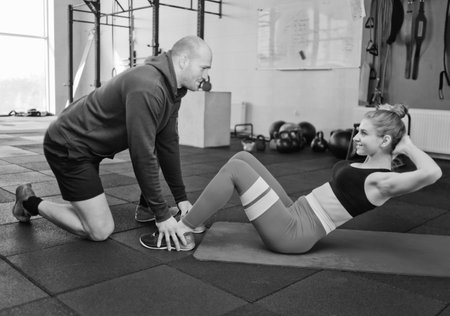 The man is holding the legs of the woman who is doing the twisting exercise for the abdominal...