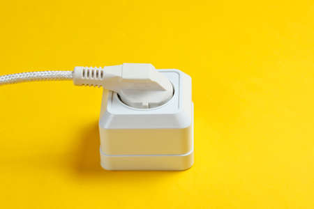White cable plugged into power outlet on yellow background