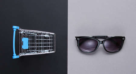 Buyer concept. Mini shopping trolley, sunglasses on paper background. Top view