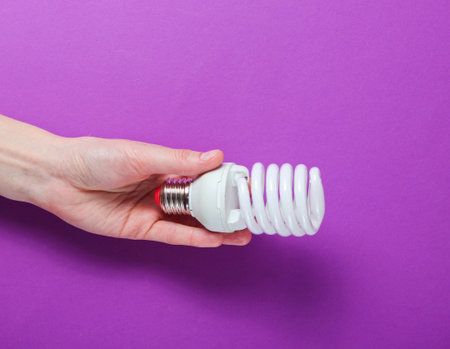 Female hand holding a spiral light bulb on purple background.