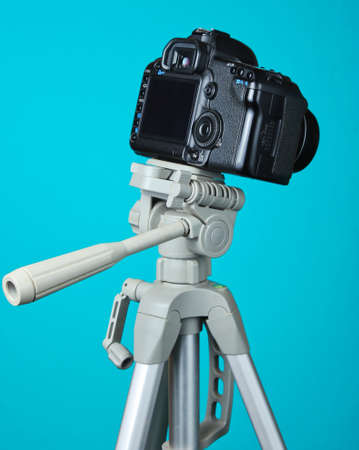 Modern digital camera with a tripod on blue backgroundの写真素材