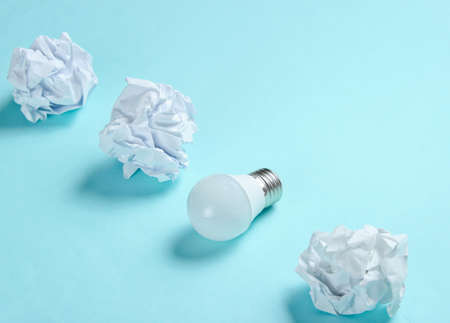 Energy saving light bulb and crumpled paper balls on blue background. Minimalistic business concept, idea.の写真素材