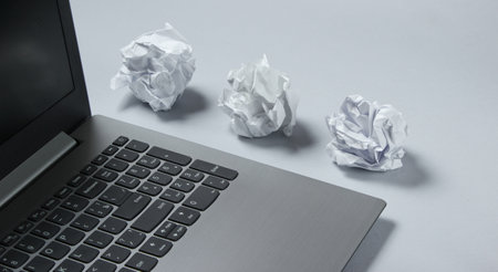 Laptop and crumpled paper balls on gray background. Minimalistic business concept.の写真素材