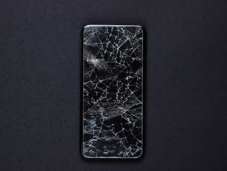 Smartphone with broken protective glass on black background