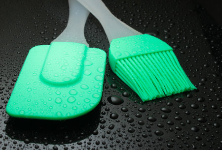 Kitchen tool in water drops on black background. Silicone spatula, brush close upの写真素材