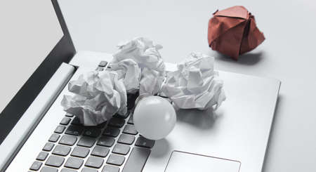 Idea business concept. Laptop, crumpled paper balls, LED light bulb on gray background