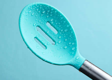 Silicone kitchen spoon colander in water drops on blue background