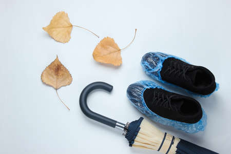 Black suede boots with boot covers, umbrella and fallen leaves on a white background. Top view....
