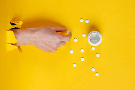 Female hand takes pill through torn yellow paper. Minimalistic creative medicine conceptの写真素材