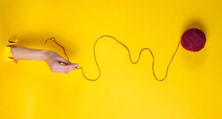 Female hand holding skein of thread through torn yellow paper. Minimalistic creative medicine...